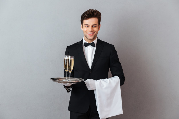 happy-young-waiter-holding-glass-champagne-towel_171337-5290